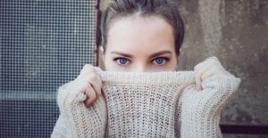 A dark-haired young woman covers her mouth with a beige knit sweater to hide her bad breath