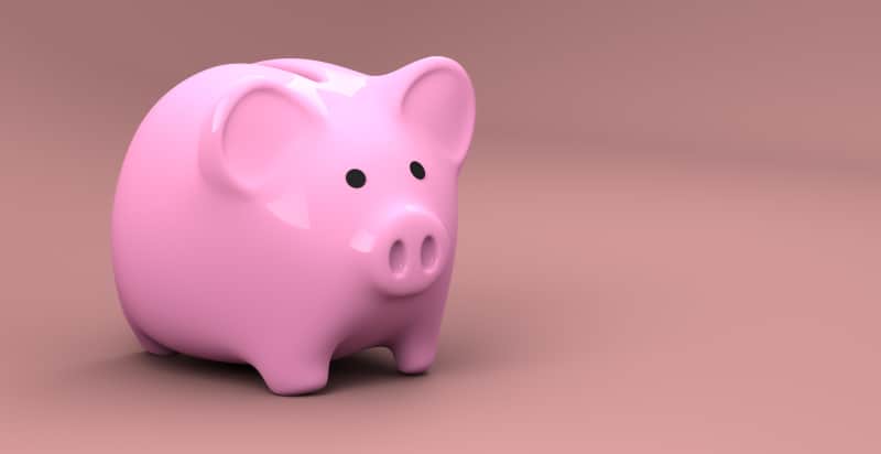 A pink plastic piggy bank for saving money stands against a darker pink background