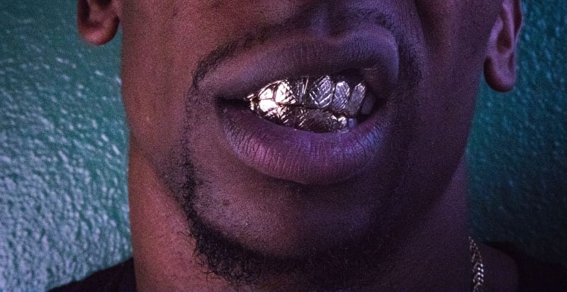 Closeup of the mouth of a man with black facial hair and wearing removable gold grills on his teeth