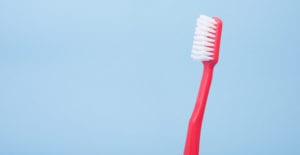 A red toothbrush with soft white bristles stands upright against a blue background