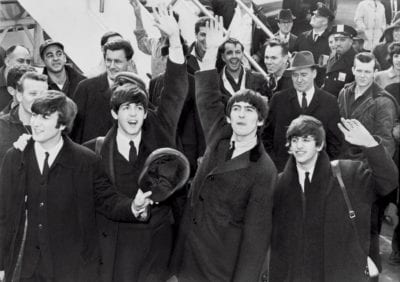 Black and white photo of the Beatles rock band in a crowd waving to fans