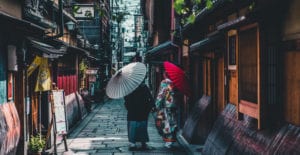 Two Japanese women, on wearing a colorful kimono, hold parasols while walking down a street in Kyoto, Japan