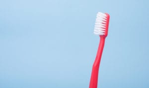 Red toothbrush with white bristles against a powder blue background