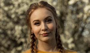 Closeup of a young woman wearing hoop earrings, a yellow blouse, and her hair in two side braids