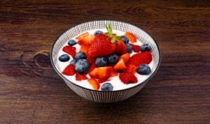 Aerial view of a bowl filled with white yogurt and fresh strawberries and blueberries on a wooden counter